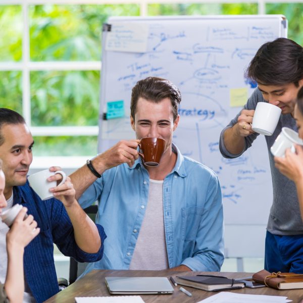 Mixed race diverse successful casual businesspeople taking break, comfortably drinking coffee together and smiling with happiness while sitting in cozy meeting room and sharing marketing idea in team. Mixed race diverse successful casual businesspeople taking break, comfortably drinking coffee together and smiling with happiness while sitting in cozy meeting room and sharing marketing idea in team
